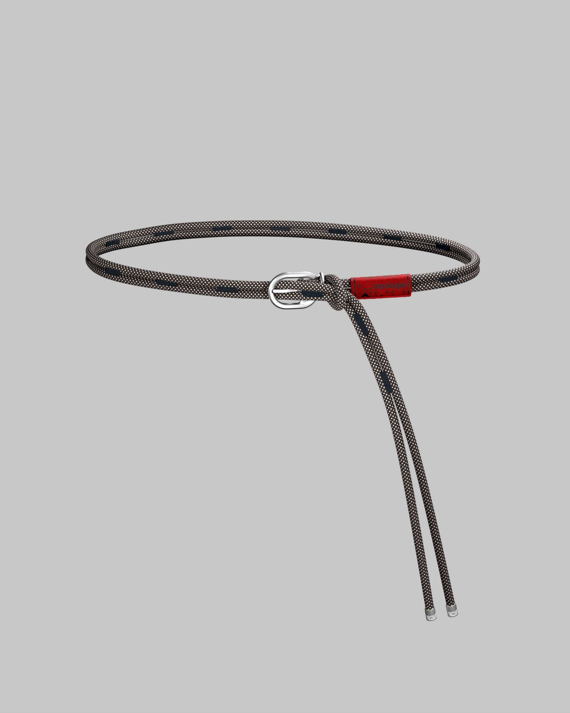 Rope Belt in sandy brown with a fine grid and navy dashes, featuring a red topologie tag and silver metal buckle, shown against a light grey background.

