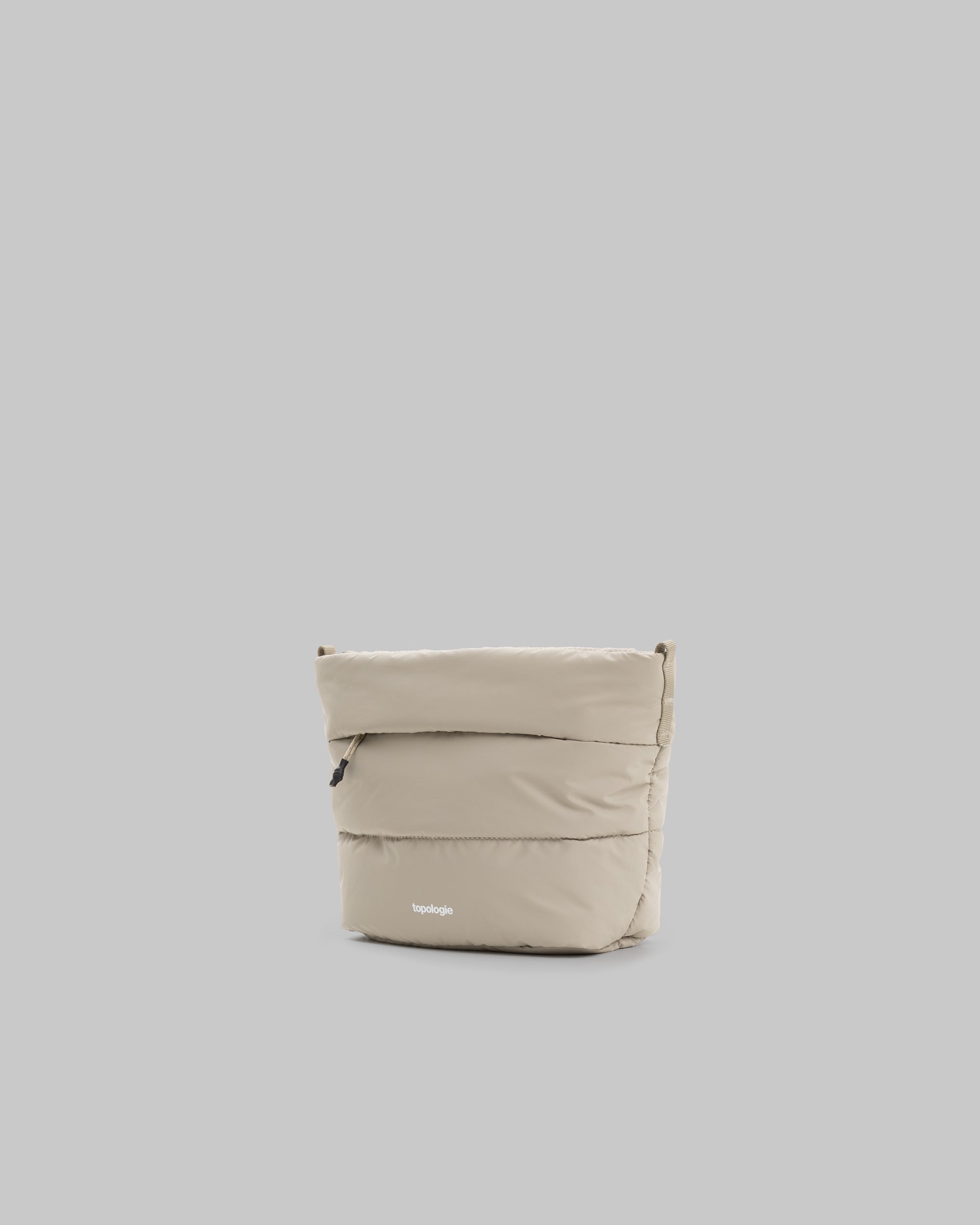 Besace in taupe quilted fabric with a front zipper and white topologie logo, shown against a light grey background.