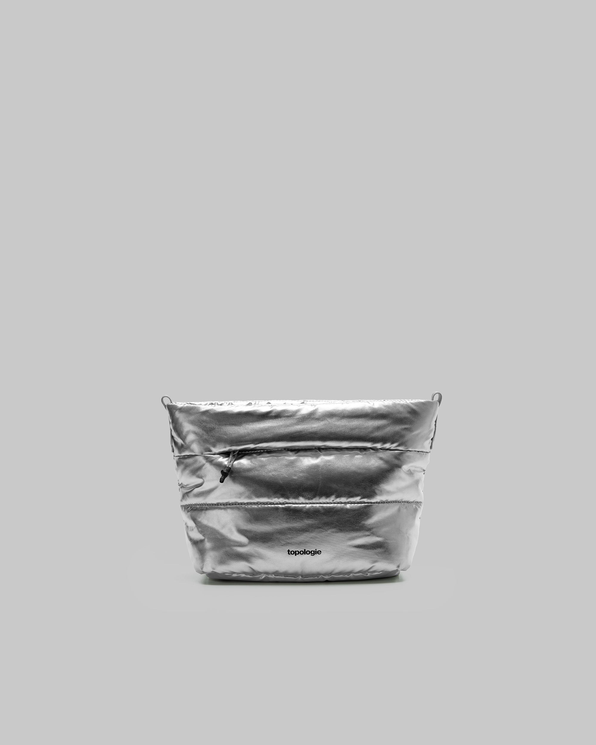 Besace in metallic silver quilted fabric with a black front zipper and topologie logo, shown against a light grey background.