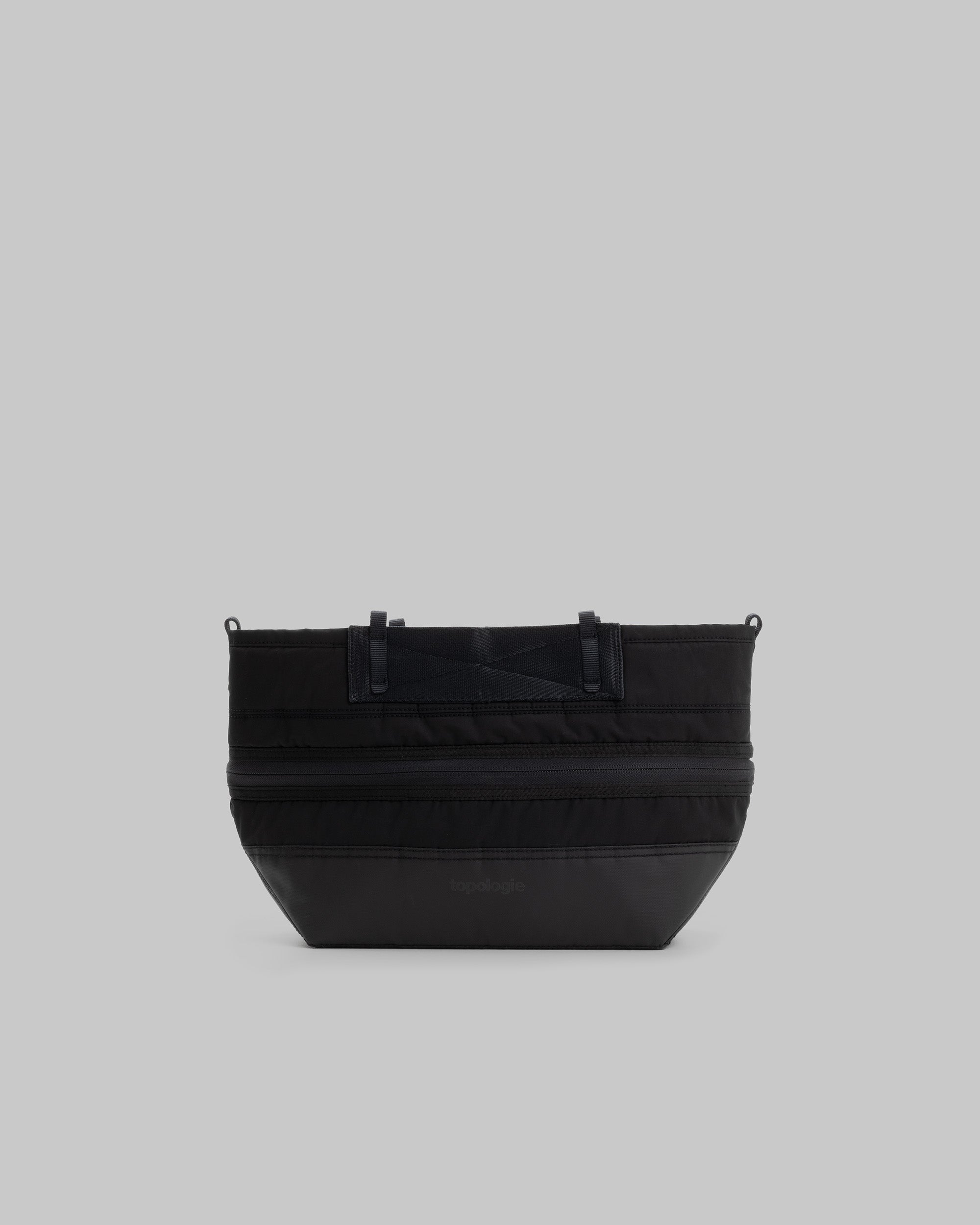 Convert Tool Bag in black quilted fabric with a horizontal zipper and matte bottom panel, shown against a light grey background.