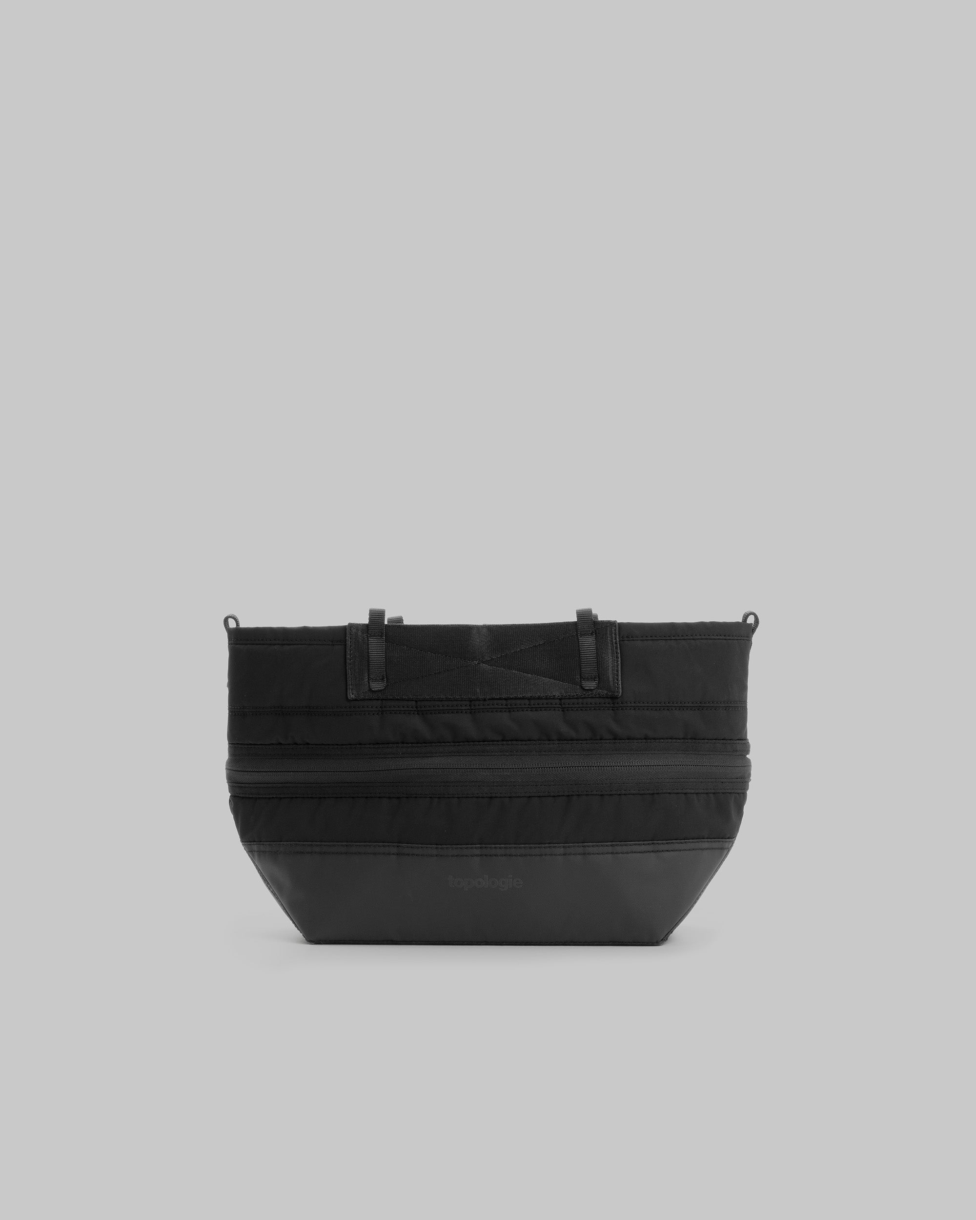 Convert Tool Bag in black matte-coated fabric with two front zippers, webbing loops, and a tonal topologie logo, shown against a light grey background.