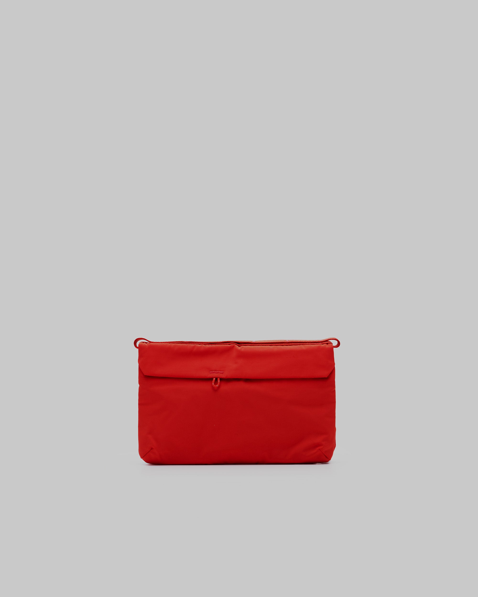 Flat Sacoche Small in bright red padded fabric with tonal loops and zipper, shown against a light grey background.