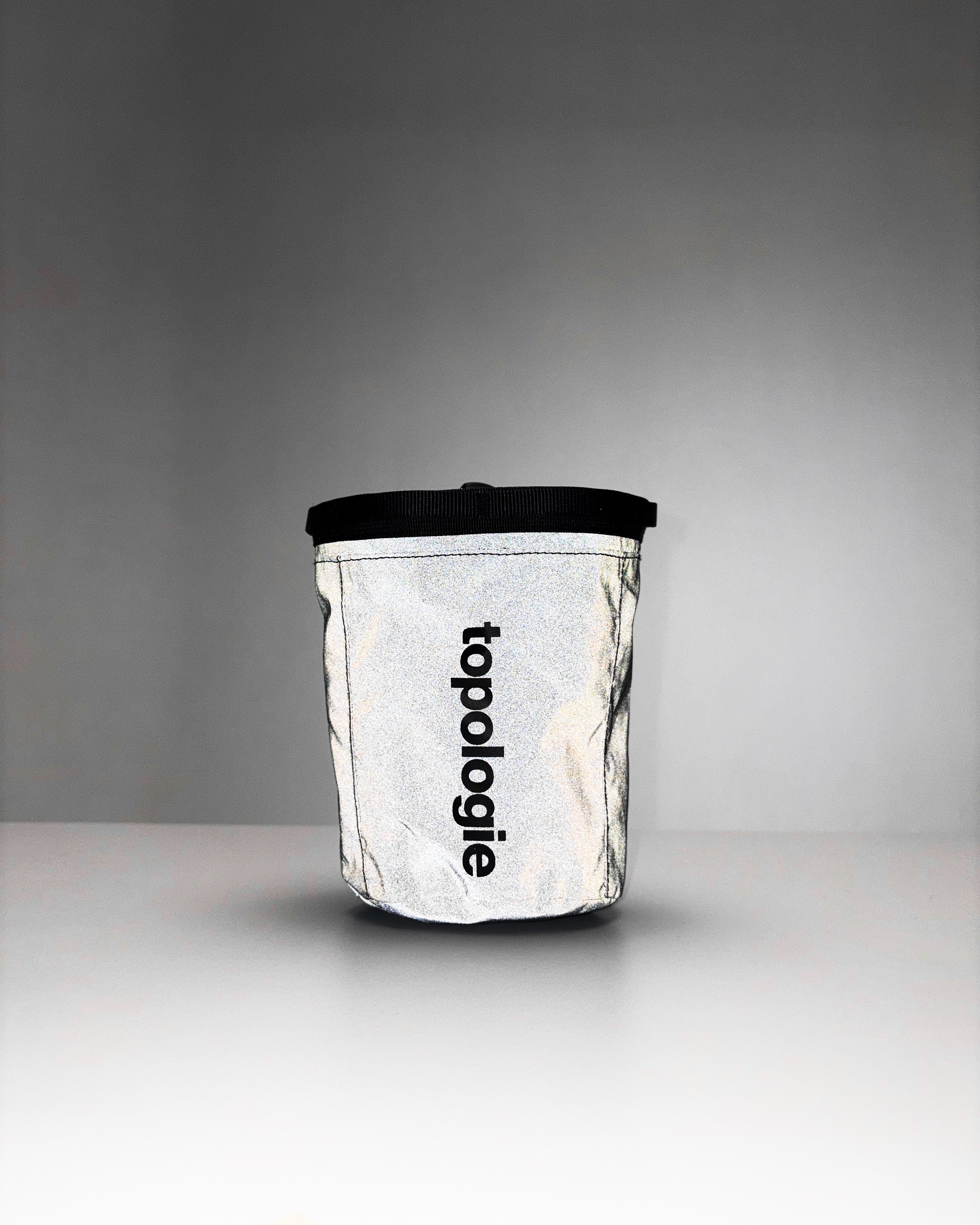Chalk Bag in reflective silver with black trim and a vertical black topologie logo, shown against a light grey background.