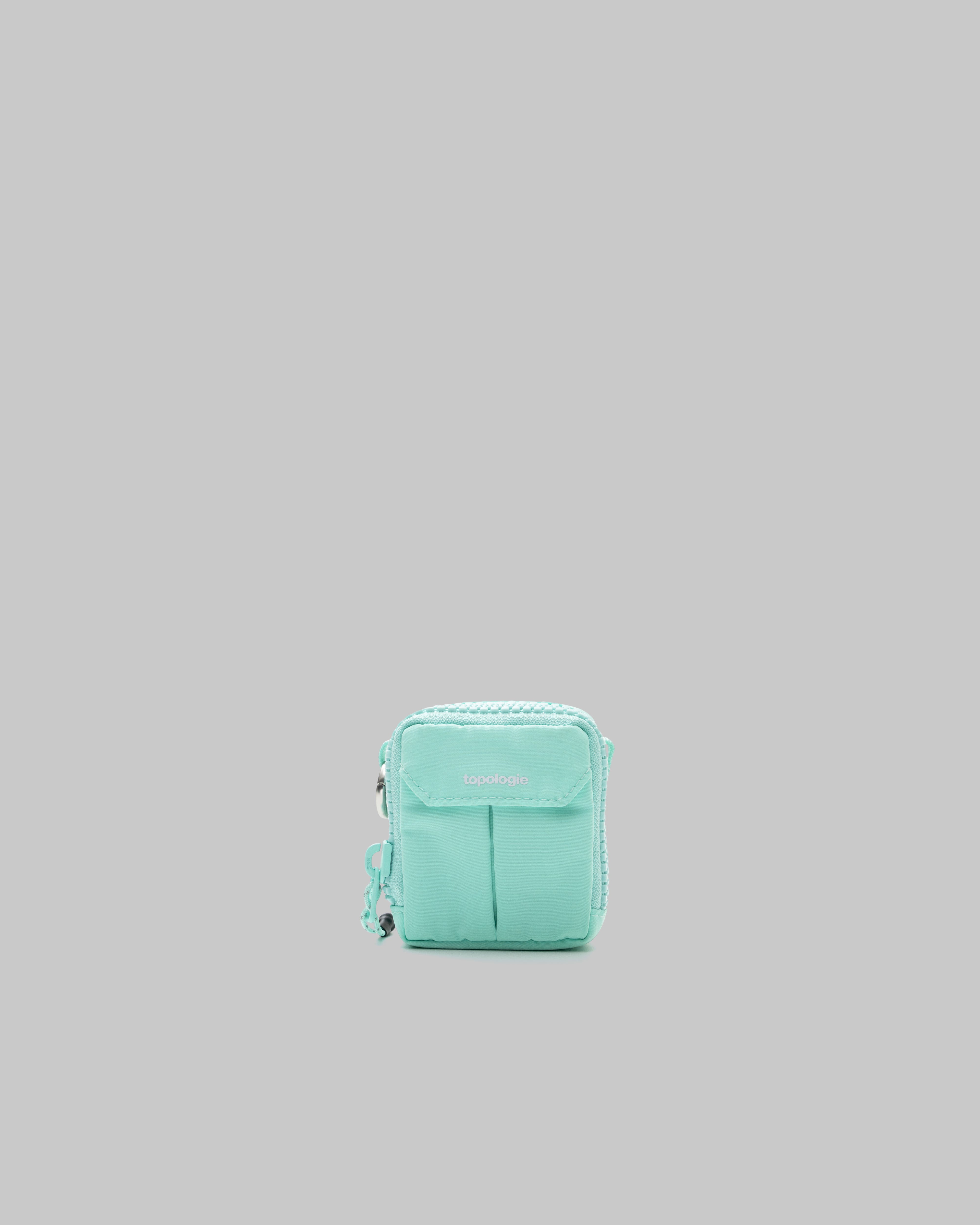 Mini Utility Sacoche in mint green with a front flap, white topologie logo, and silver side ring, shown against a light grey background.