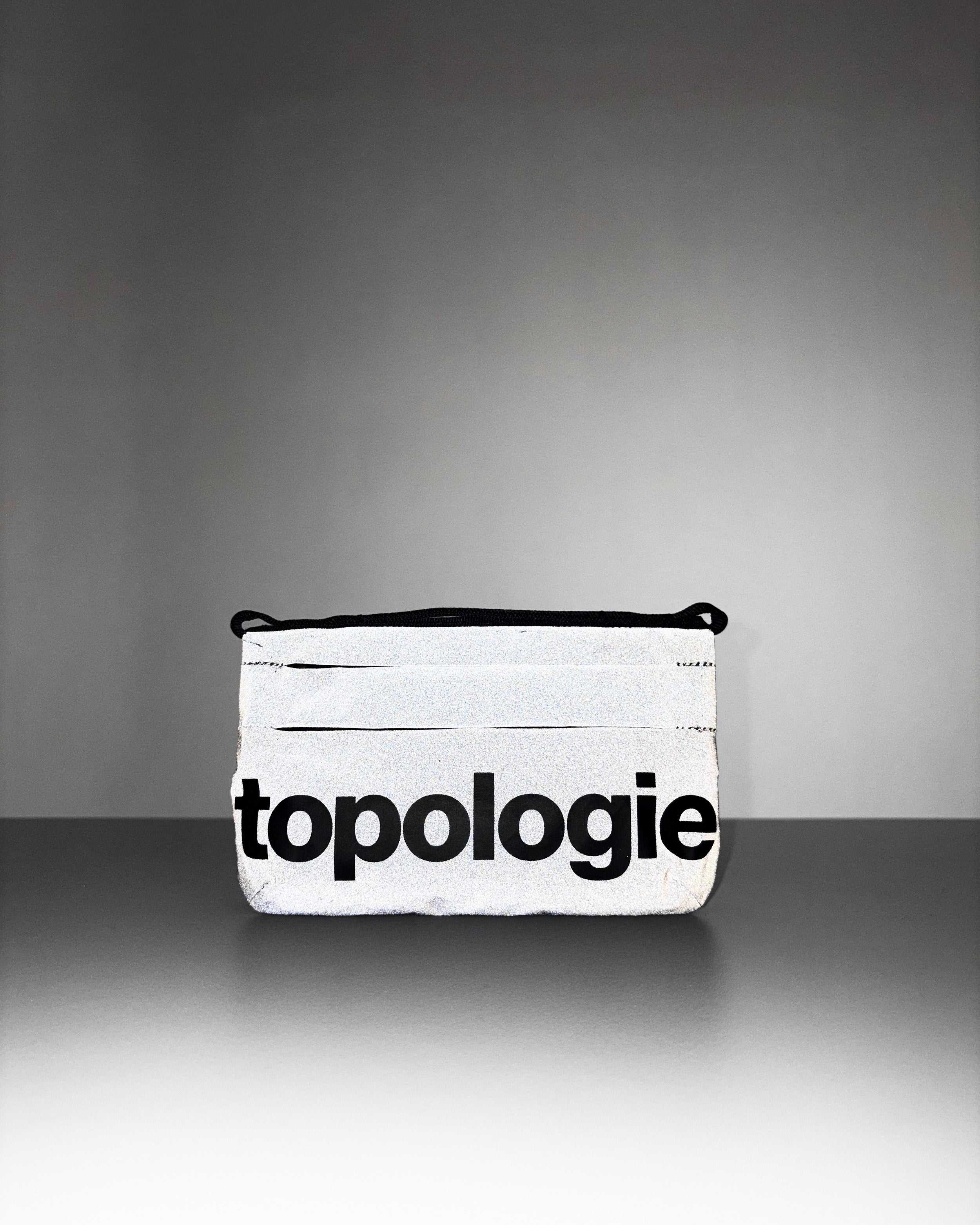 Phone Sacoche 90 in silver reflective fabric with a large black topologie logo, shown against a light grey background.
